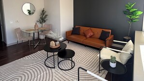 A modern living room with a ceiling fan, a round mirror, a sofa, a coffee table, and a dining area with a glass table. - Cozy 1-bedroom apartment in amazing Downtown Dallas sleeps 4 (Dallas)