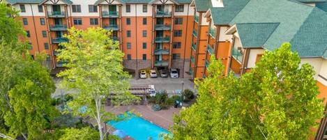 A multi-story hotel with a swimming pool, surrounded by lush greenery.