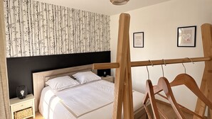 A bedroom with a bed, wooden headboard, nightstands, a hanging light fixture, and a wall with vertical stripes.