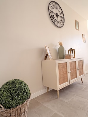 A hallway with a white cabinet, a large wall clock, and a potted plant.