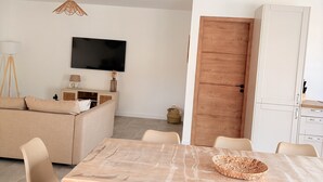 A modern living room with a sofa, TV, wooden door, and a dining table with chairs.
