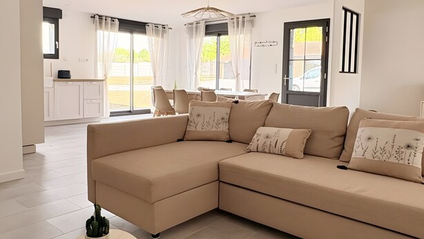 A modern living room with a beige sectional sofa, a round coffee table, and a view of the outside.