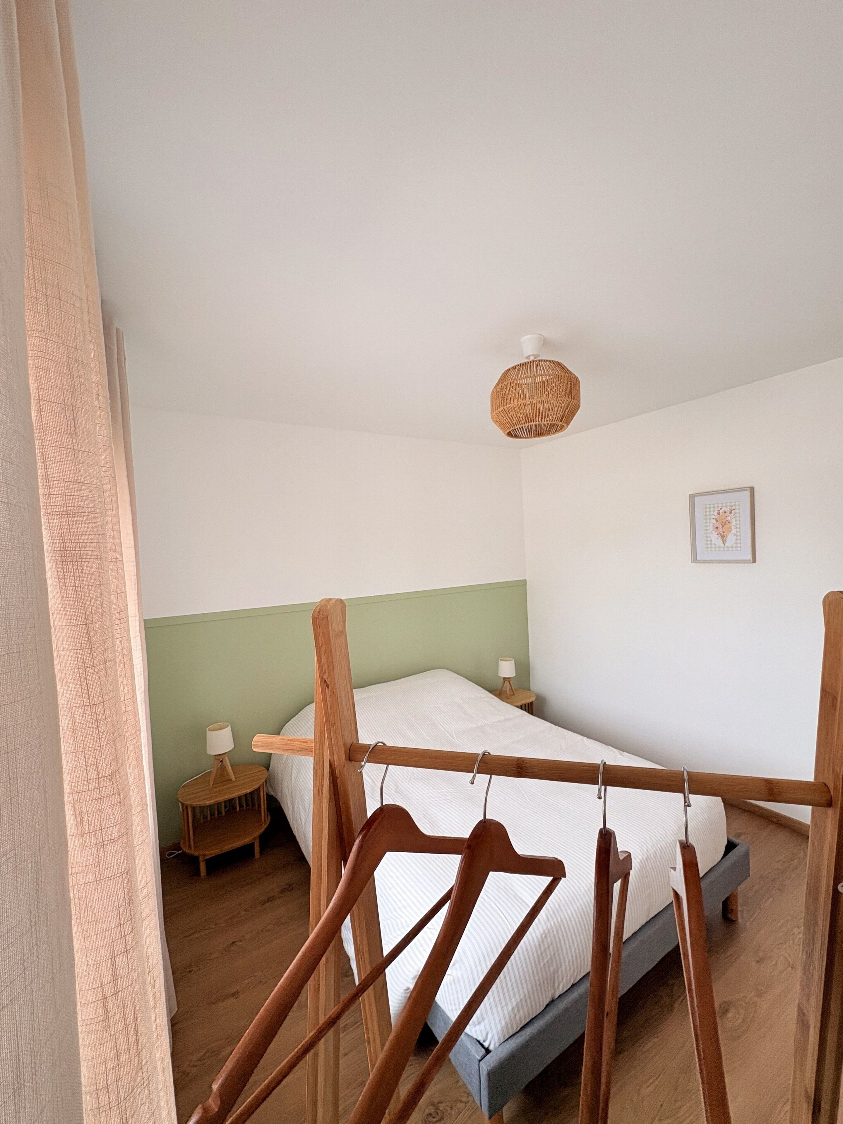 A bedroom with a bed, a bedside table, a hanging light fixture, and a framed picture on the wall.
