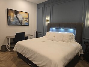 Une chambre à coucher avec un lit, un bureau, une chaise et un tableau accroché au mur.