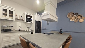 Una cucina moderna con mobili bianchi, un'isola centrale con sgabelli da bar, un forno a microonde e un frigorifero.