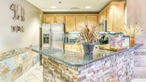 A kitchen with granite countertops, a refrigerator, wooden cabinets, and decorative plants. - Baskins Creek 201 (Gatlinburg)