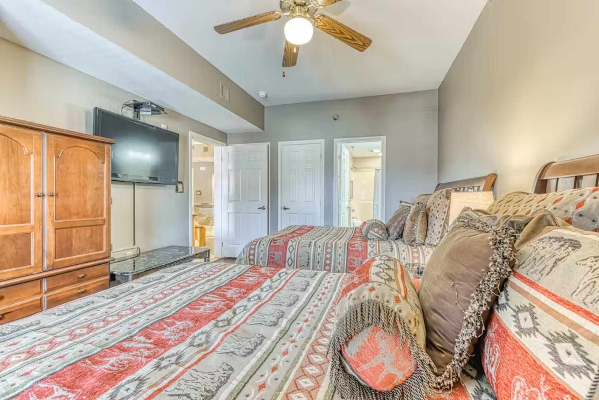 A bedroom with a bed, a wooden wardrobe, a ceiling fan, and a television.