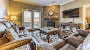 A living room with a stone fireplace, a flat-screen TV, a sofa, and a coffee table. - Baskins Creek 201 (Gatlinburg)