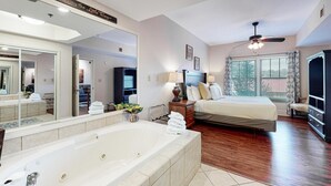 A hotel room with a large mirror, a bathtub, a bed, a ceiling fan, and a view of the outdoors. - Baskins Creek 203 (Gatlinburg)