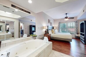 Ein Hotelzimmer mit großem Spiegel, einer Badewanne, einem Bett, einem Deckenventilator und Blick ins Freie.