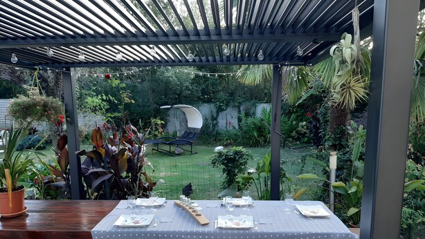 Un pati exterior amb una taula preparada per dinar, envoltat de verdor exuberant i vistes al jardí.