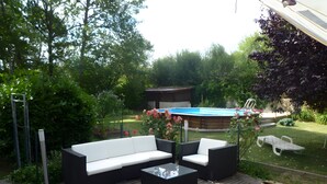Zona d'estar exterior amb sofà i cadires, una piscina i un jardí.