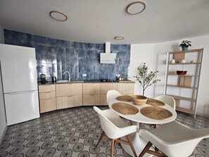A modern kitchen with a curved countertop, a white refrigerator, and a dining area with a round table and white chairs.
