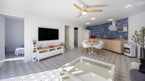 Una sala de estar moderna con televisor, zona de estar y una cocina al fondo.