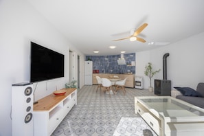 A modern living room with a flat-screen TV, a wooden coffee table, a glass-top coffee table, a sofa, and a ceiling fan.