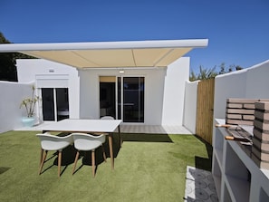 A modern outdoor patio with a white table and chairs, a barbecue grill, and a covered seating area.
