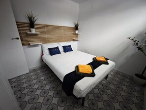 A bedroom with a bed, two bedside tables, a headboard, and a potted plant.