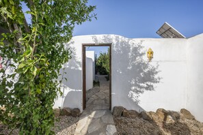 Un sendero conduce a la entrada de un edificio, rodeado de muros blancos, un camino de piedra y un pequeño jardín.