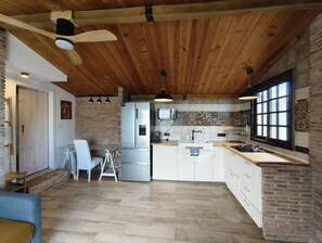 A kitchen with wooden ceiling beams, a refrigerator, a microwave, and a window with blinds.
