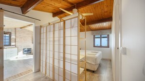 A room with a wooden ceiling, a bed, a window, and a view of a brick wall.