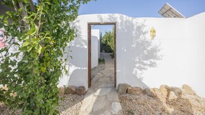 A pathway leading to a white building with a stone entrance, surrounded by rocks and greenery.