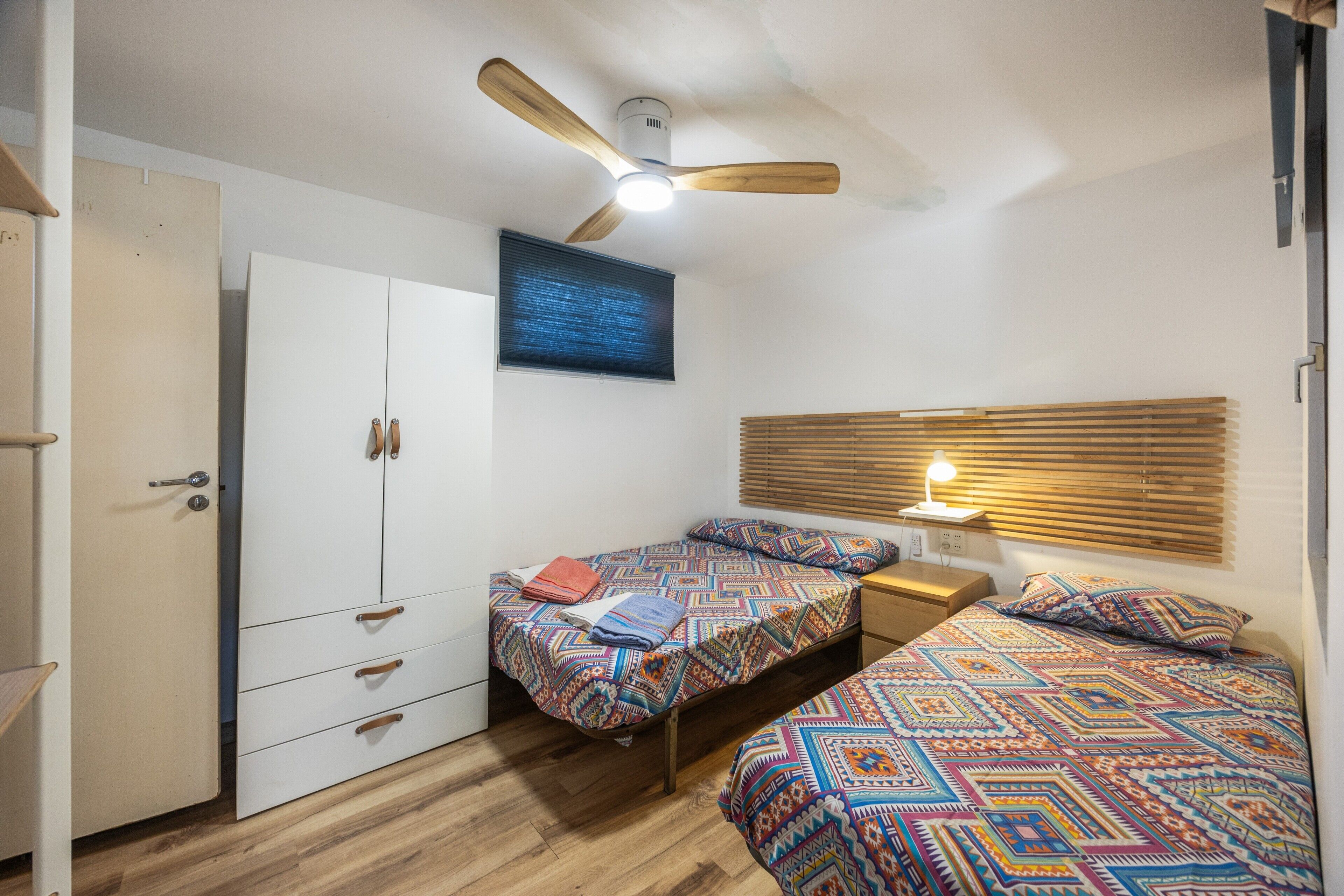 A bedroom with two beds, a wardrobe, a ceiling fan, and a window with blinds.