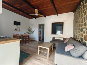 A living room with a wooden ceiling, a stone wall, a sofa with cushions, a wooden table, and a TV mounted on the wall.