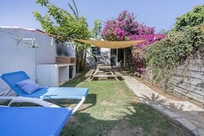 Un patio trasero con dos sillones azules, una terraza de madera y un jardín con flores moradas.