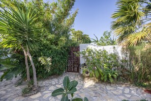 Un jardín empedrado con plantas tropicales y una entrada con portón.