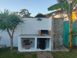 A small outdoor area with a white wall, a brick barbecue grill, a potted plant, and a trash bin.