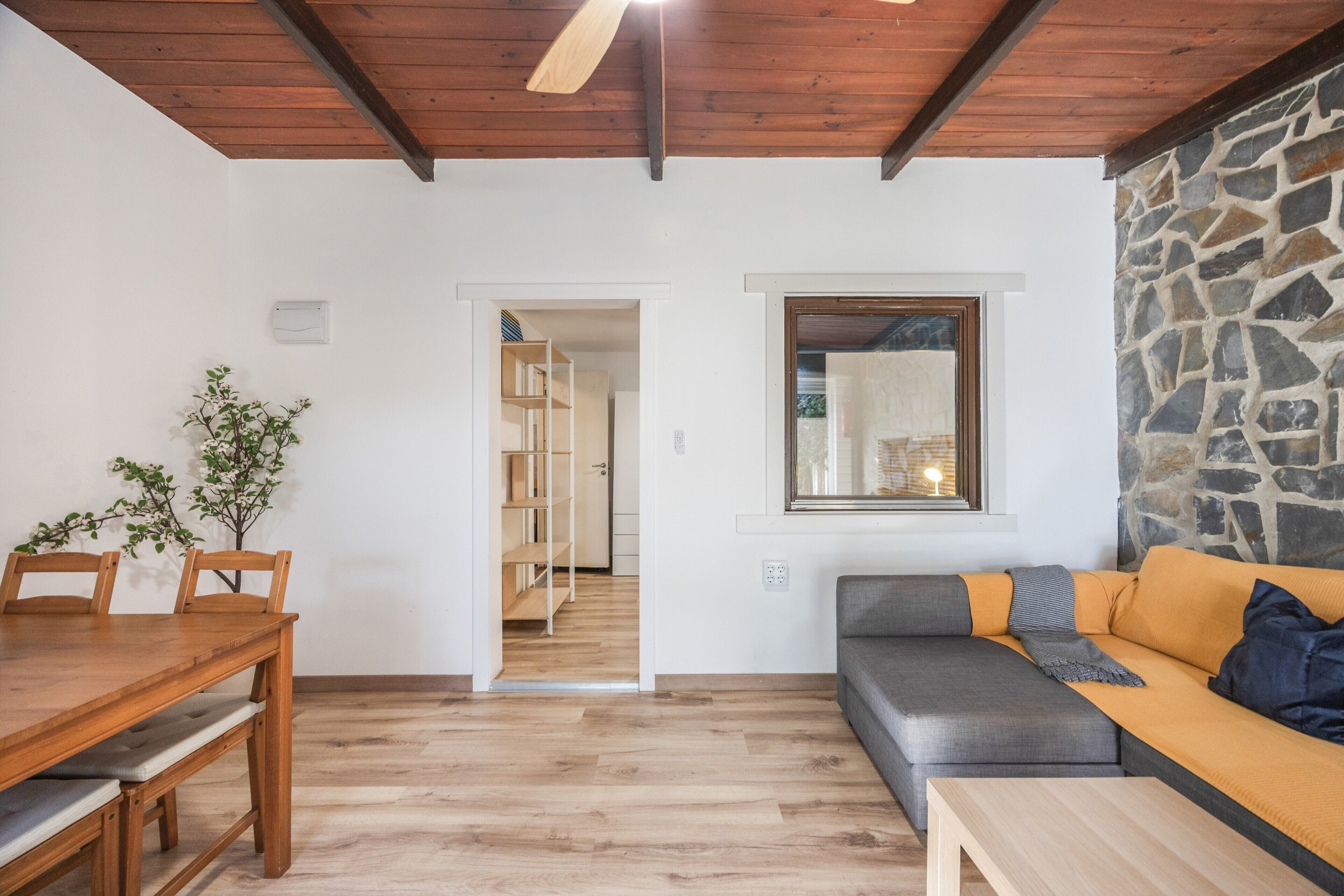 Un salon moderne avec une table à manger en bois, un canapé gris, un banc en bois et un mur en pierre.