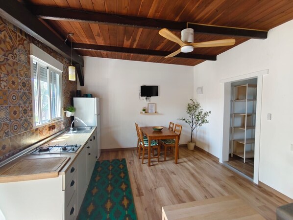 A compact kitchen with a wooden ceiling, a dining area with a table and chairs, and a small potted plant.
