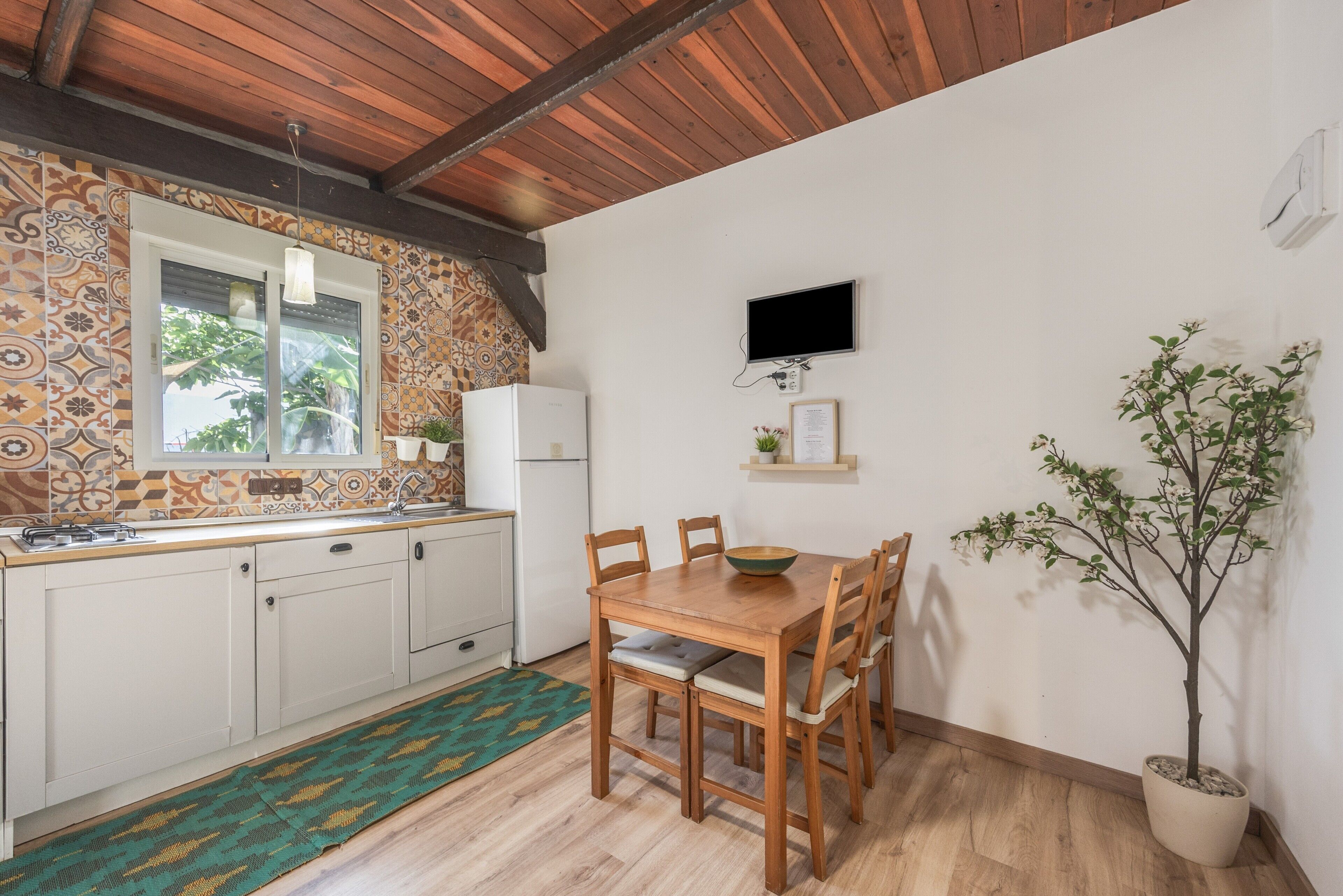 A kitchen with a wooden table and chairs, a window, a television, and a potted plant.