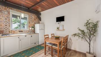 Een keuken met een houten tafel en stoelen, een raam, een televisie en een potplant.
