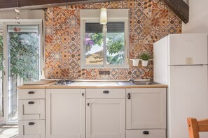 Una cocina con baldosas estampadas, un ventanal con una lámpara colgante, un lavamanos y un refrigerador.