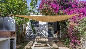 A patio with a wooden table and chairs, a stone wall, and a hanging shade cloth. - Casa Oasis with Private Garden in El Palmar, 5 Minutes from the Beach (El Palmar de Vejer)
