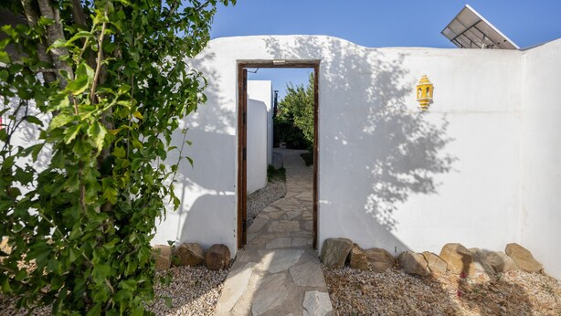 A pathway leading to a white building with a door, surrounded by rocks and greenery. - Casa Pequeña Lulú - Sunwaves, just 5 minutes’ walk from the beach (El Palmar de Vejer)
