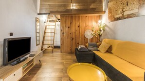 A living room with a TV, wooden floor, yellow sofa, and a fan. - Casa Pequeña Lulú - Sunwaves, just 5 minutes’ walk from the beach (El Palmar de Vejer)