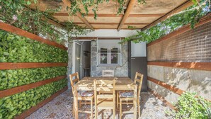 A covered patio with a wooden table and chairs, surrounded by a stone wall and a wooden fence. - Casa Pequeña Lulú - Sunwaves, just 5 minutes’ walk from the beach (El Palmar de Vejer)