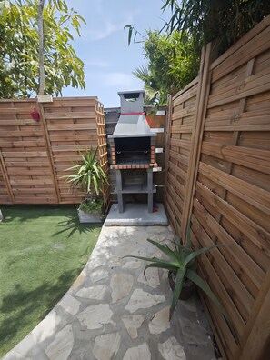 Un jardin avec un barbecue, un chemin de pierres et des clĂŽtures en bois.