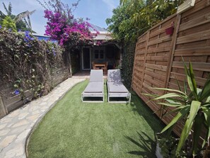 A garden with a wooden fence, a stone pathway, and a small seating area with two lounge chairs.