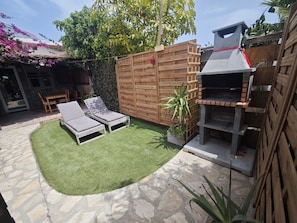 A backyard with two lounge chairs, a barbecue grill, and a stone patio.