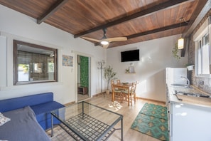 Un salon avec un canapé bleu, une table basse en verre, un plafond en bois, un coin repas avec une table et des chaises, et un coin cuisine avec un évier et un plan de travail.