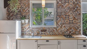 Une cuisine avec des carreaux décoratifs, un luminaire suspendu, un évier et une fenêtre donnant sur un paysage verdoyant.