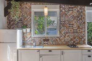 Cocina con baldosas estampadas, una lámpara colgante, un lavamanos y una ventana con vistas a la vegetación.