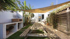 A wooden patio with a table and chairs, surrounded by a white wall and a wooden fence, with potted plants and a clear sky. - Casa Marina - Sunwaves El Palmar, 5 min from the beach, private garden & Wi-Fi (El Palmar de Vejer)