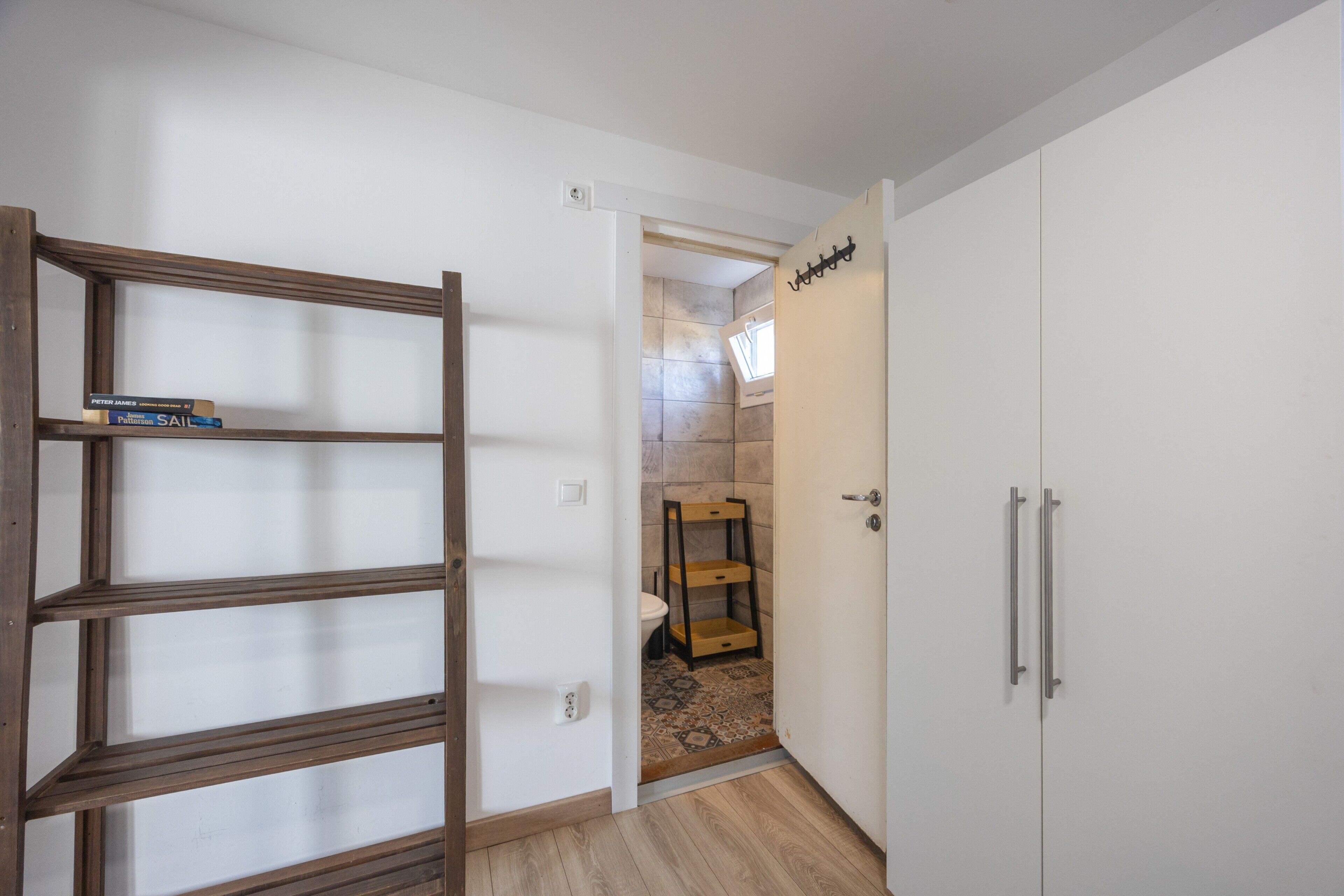 Un pasillo con una escalera de madera, una puerta blanca con picaporte y un muro cubierto de azulejos.