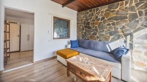A living room with a stone wall, wooden ceiling, and a sofa with cushions. - Casa Marina - Sunwaves El Palmar, 5 min from the beach, private garden & Wi-Fi (El Palmar de Vejer)
