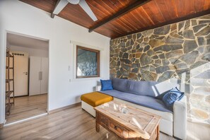 A living room with a stone wall, wooden ceiling, and a sofa with cushions. - Casa Marina - Sunwaves El Palmar, 5 min from the beach, private garden & Wi-Fi (El Palmar de Vejer)