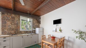A kitchen with patterned tiles, a wooden ceiling, a dining table with chairs, a TV on the wall, and a small shelf with a plant. - Casa Marina - Sunwaves El Palmar, 5 min from the beach, private garden & Wi-Fi (El Palmar de Vejer)